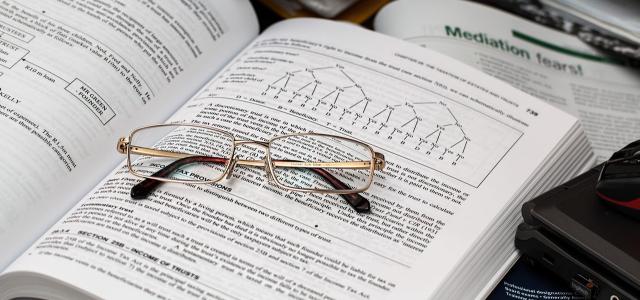 A pair of reading glasses sitting on an open textbook. The book has content on taxes.